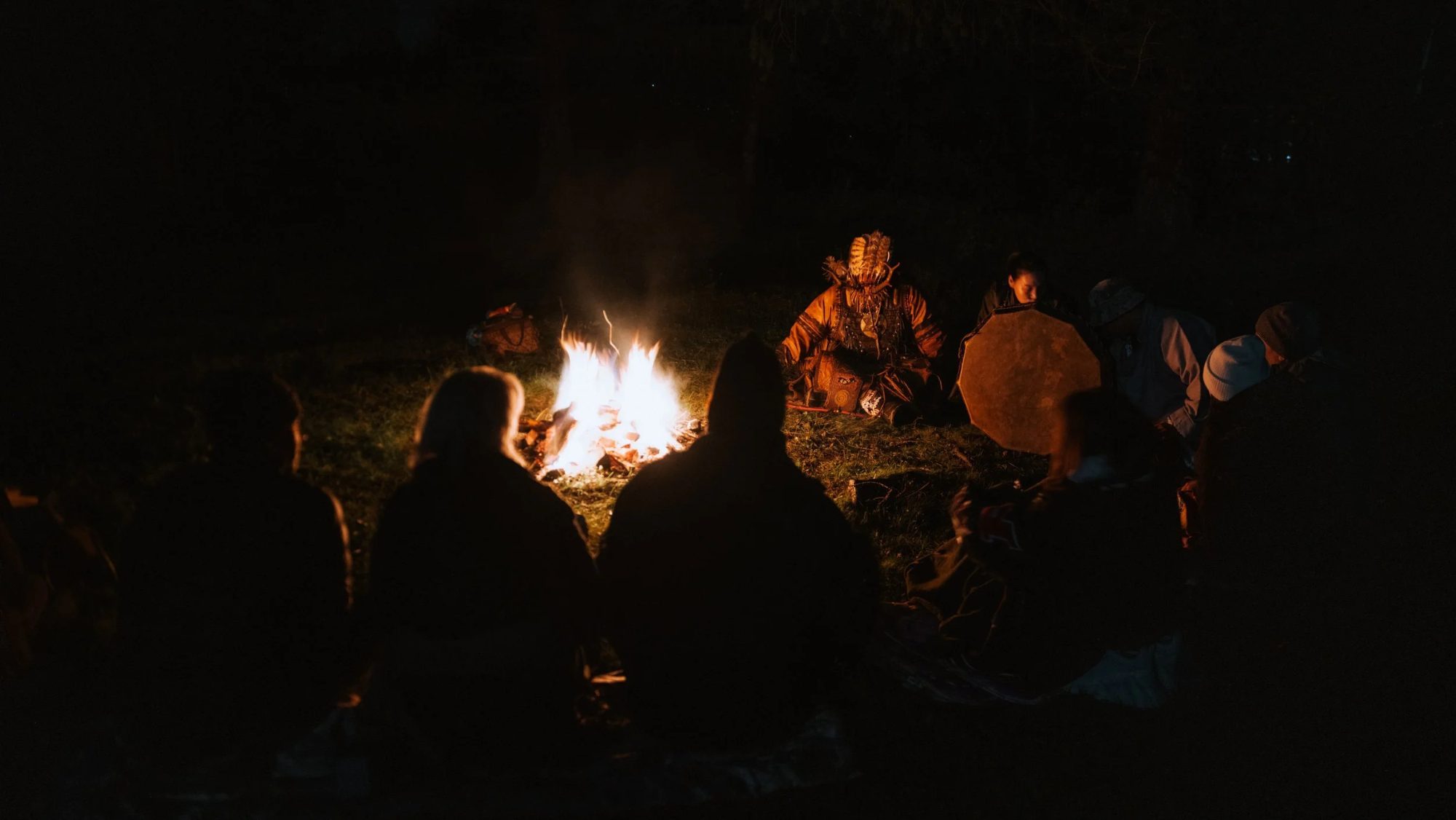 Travellers gathered around a fire with a shaman at night