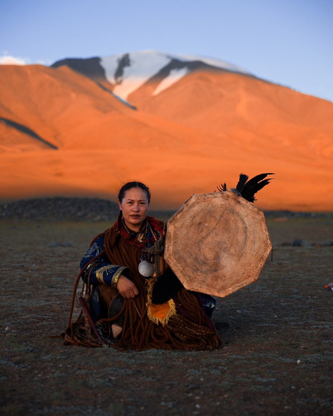 Mongolian shaman seated with her drum before a sunlit mountain