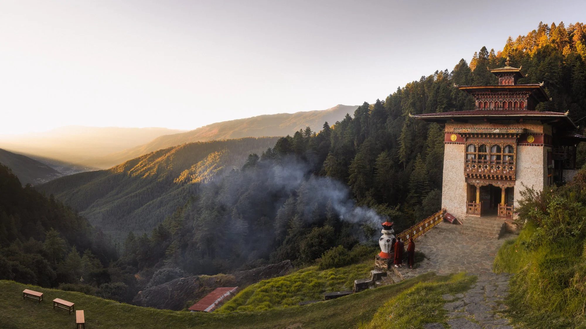 Monks at a Bhutanese temple above a forested valley at dawn
